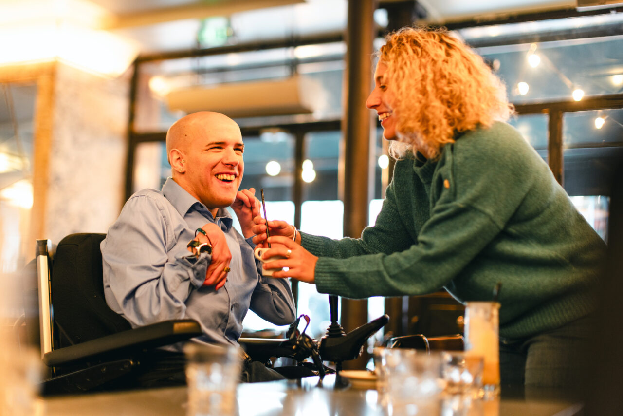 Mickael atteinte de l'infirmité motrice cérébrale aidé par son auxiliaire de vie pour boire son verre