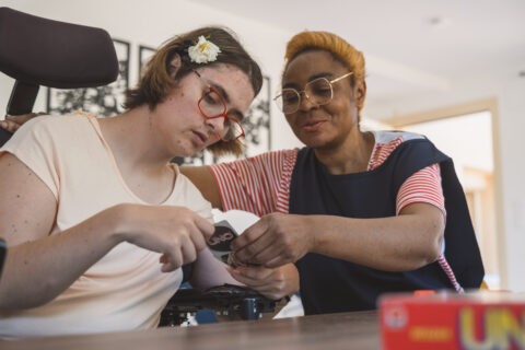 une bénéficiaire en fauteuil roulant joue aux cartes avec son auxiliaire de vie.